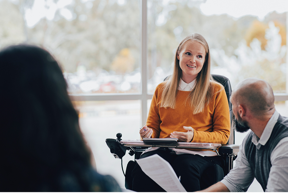 Une femme est assise dans un fauteuil roulant lors d'une réunion de travail.